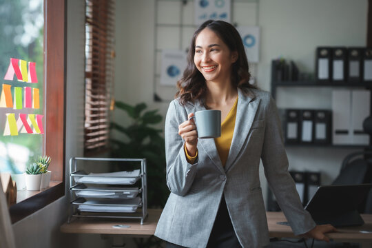 Beautiful Asian business woman standing smiling confident and bright looking ready to work in the new day with a cup of coffee. Please be ready to work.