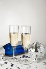 Glasses of champagne, bottle, Christmas balls and confetti on light background