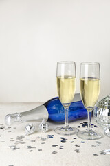 Glasses of champagne, bottle, Christmas balls and confetti on light background