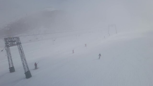 Aerial flyover Skier skiing snowy slope during foggy day beside ski lift in Austria 