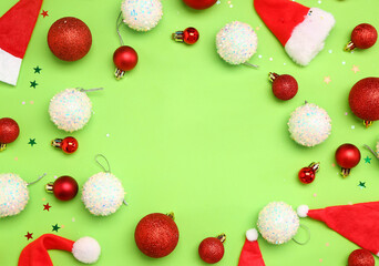 Frame made of beautiful Christmas balls and Santa hats on green background