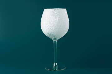Decorative snow-covered frosted wine glass on green background