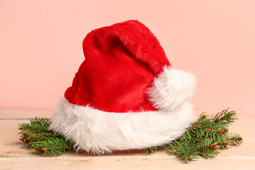 Obraz na płótnie Canvas Santa hat with fir branches on light wooden table against pink background