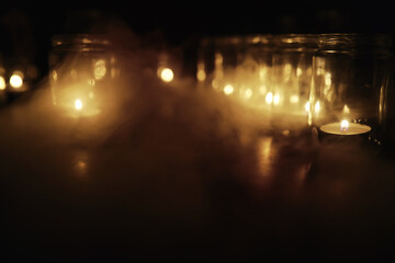 Fototapeta na wymiar Background with candles in glass vessels. Candles burn in a dark place. Rest in peace.