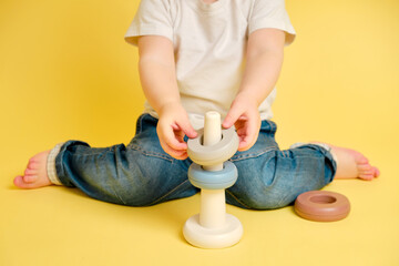 Toddler baby is playing logic educational games with a pyramid on a studio yellow background. Happy child playing with a pyramid educational toy, learning logic. Kid aged one year four months