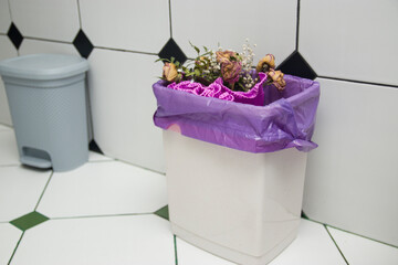 Waste bin full of old discarded flowers. Flowers in the trash, bouquet in the urn, discarded bouquet