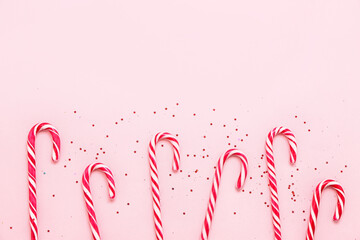 Composition with tasty candy canes and sequins on pink background