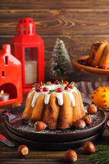 Plate with tasty Christmas cake and hazelnuts on wooden table