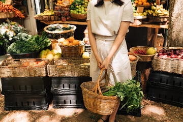 Cropped of an unrecognizable woman holding a wicker basket with vegetables standing at a stall on a farmer's market with organic food