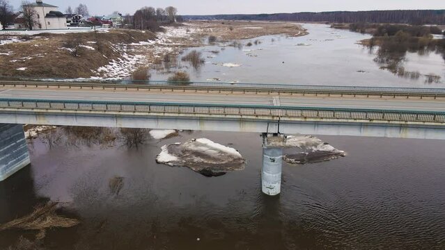 Automobile bridge across a muddy river stream with floating ice floes. Spring, snow melts, ice drift, flood and flood of the river. Day, cloudy weather, soft warm light. UHD 4K