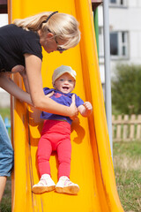 Fototapeta na wymiar Happy family moments, mother catching toddler daughter getting down the slide in summer in the park
