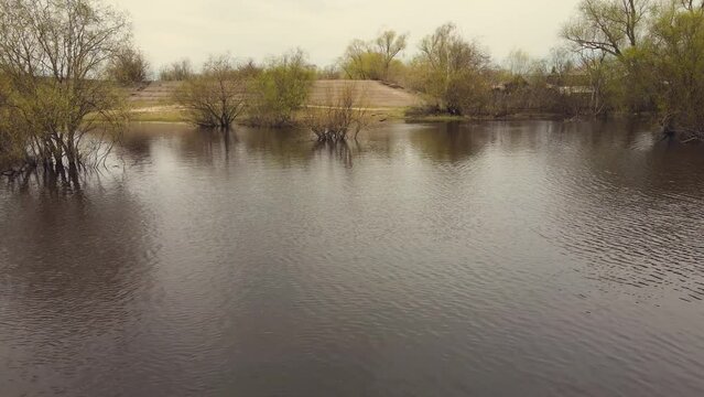 Wide spring flood, river overflow, flooded trees, aerial view. Snow is melting, high water levels, flooded banks, fields, trees. Warm cloudy day, soft light. UHD 4K.