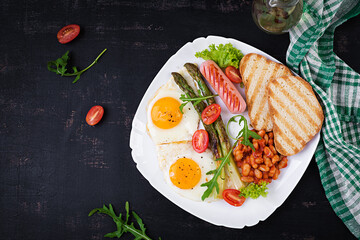 Keto breakfast. Breakfast. Fried eggs, bread toast, green asparagus, beans and sausage on white plate. Top view, flat lay