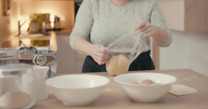 Senior woman cook unwraps foil cuts pasta dough kitchen in close up