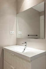 Simple, empty and modern bathroom with beige tiles, sink and mirror