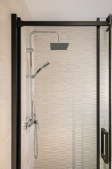 Modern tiled bathroom with rain head, hand held shower and glass door with black framing.