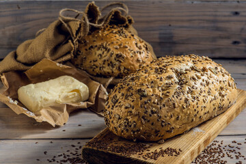 Artisan bread, natural wholegrain. It lies on an old wooden table next to other groceries. Rustic composition, rural atmosphere. Old boards and flax as background