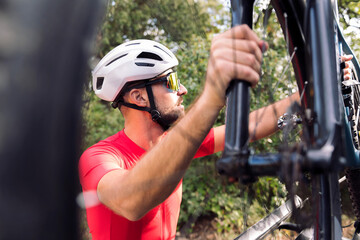 Fototapeta premium young man in helmet and cycling clothes taking his mountain bike off the bike rack of his van to go for a training ride, concept of freedom and sport in nature