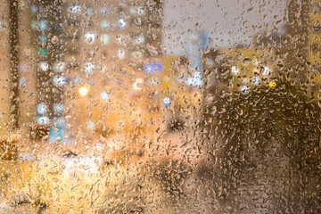 Frozen raindrops on the glass, raindrops on the window. In the background, a blurry plan, at home, in the windows, there is light with a bokeh effect.