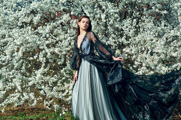 Portrait of a young beautiful girl in a spring blooming garden. Woman in an evening designer dress