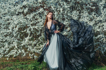 Portrait of a young beautiful girl in a spring blooming garden. Woman in an evening designer dress