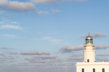 White lighthouse on a blue sky with gray clouds at sunset.