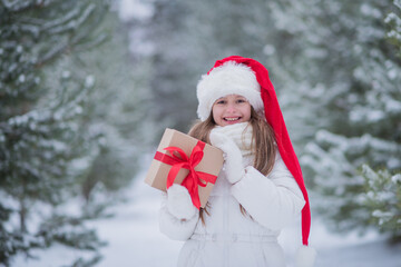 portrait of a happy girl in a Santa hat with a gift box in her hands in nature in a winter park, happy Christmas