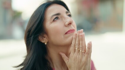 Middle age hispanic woman praying with closed eyes at street