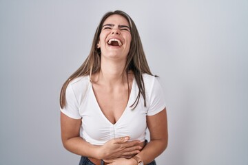 Young beautiful woman wearing casual white t shirt smiling and laughing hard out loud because funny crazy joke with hands on body.