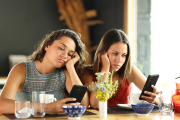 Bored friends checking phones in a restaurant