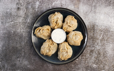 Manti steamed Dumplings with meat and potatoes with sauce on a round plate on a dark gray background. Top view, flat lay