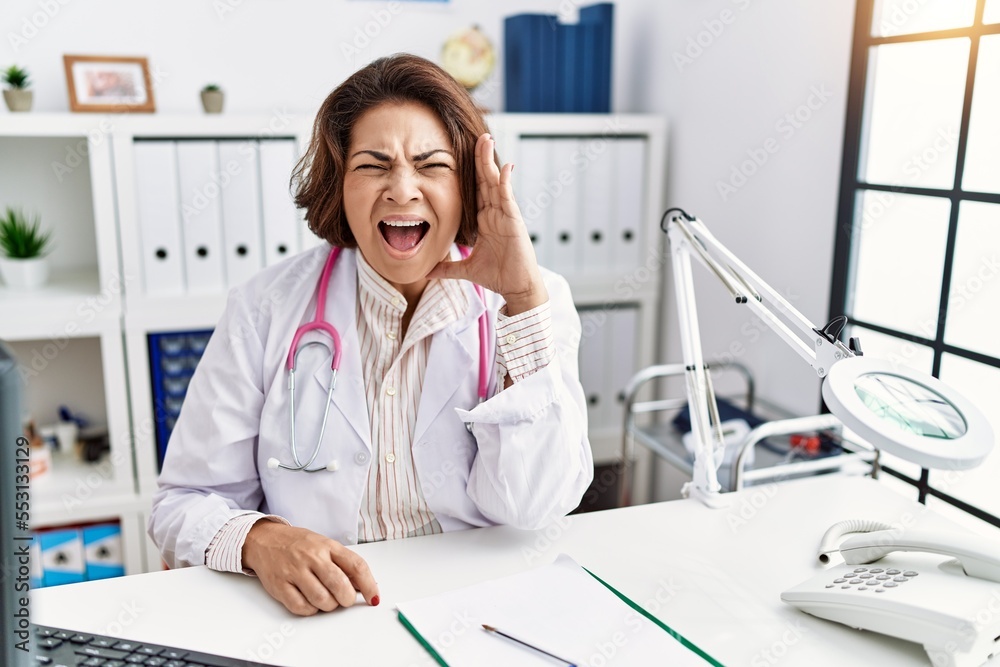 Poster middle age hispanic woman wearing doctor uniform and stethoscope at the clinic shouting and screamin