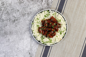 Red-Braised Pork Belly with rice and herbs on a white square  plate on a dark background. Top view, flat lay`