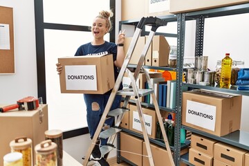 Young caucasian woman volunteer holding donations box smiling with happy face winking at the camera...