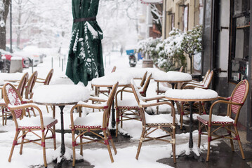 Winter in a city, street covered by snow, beautiful snowy winter scene on town with cafe tables covered by snow