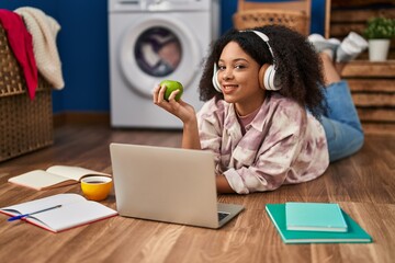 Young african american woman waiting for washing machine studying and eating apple at laundry - Powered by Adobe