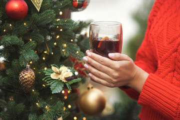 Woman in a red sweater warms her hands and holding a glass of hot wine at the Christmas market in the city