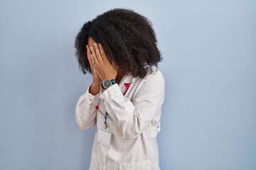 Young african american woman wearing doctor uniform and stethoscope with sad expression covering face with hands while crying. depression concept.