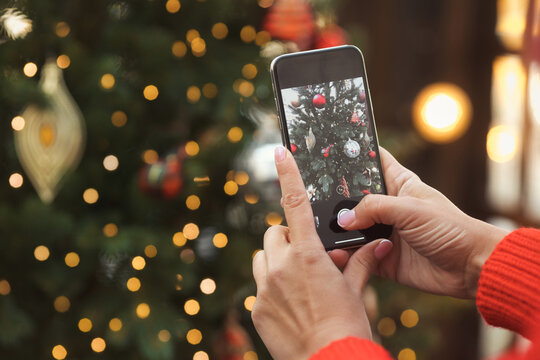 Woman hands holding a mobile phone and makes a photo of beautiful Christmas decorations with lights. Copy space.