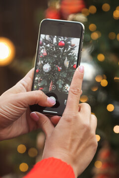 Close photo of female hands taking a picture of a decorated Christmas tree on a phone