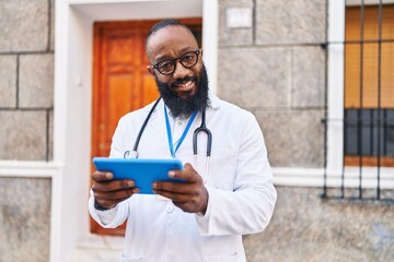 Young african american man wearing doctor uniform using touchpad at hospital