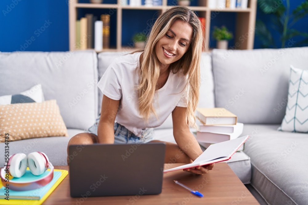 Sticker Young blonde woman student sitting on sofa reading notebook at home