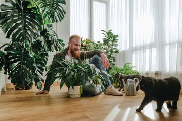 Smiling man sitting with plant looking at cat