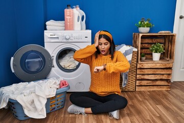 Young hispanic woman doing laundry looking at the watch time worried, afraid of getting late
