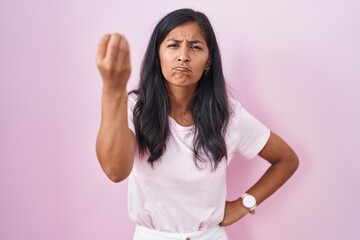 Young hispanic woman standing over pink background doing italian gesture with hand and fingers confident expression