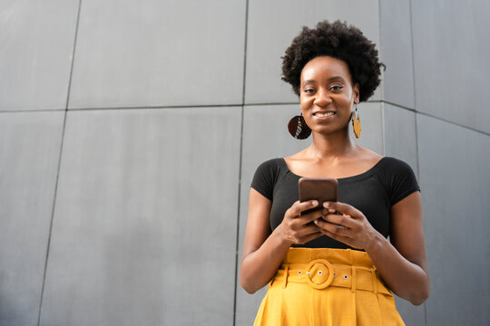 Happy Woman With Smart Phone Standing In Front Of Gray Wall