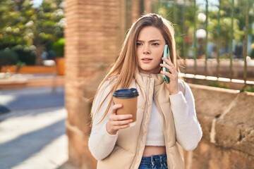 Young blonde woman talking on the smartphone drinking coffee at street