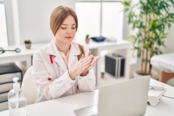 Young blonde woman wearing doctor uniform using sanitizer gel hands at clinic