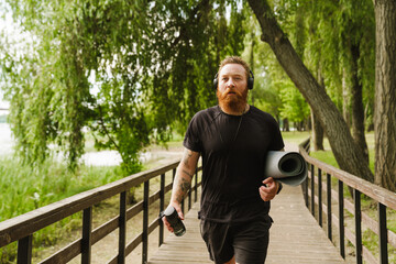 Ginger bearded sportsman listening music while walking in park