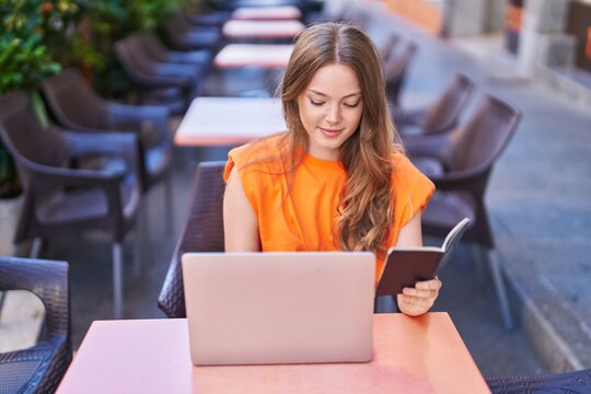 Young woman using laptop hiolding passport at coffee shop terrace